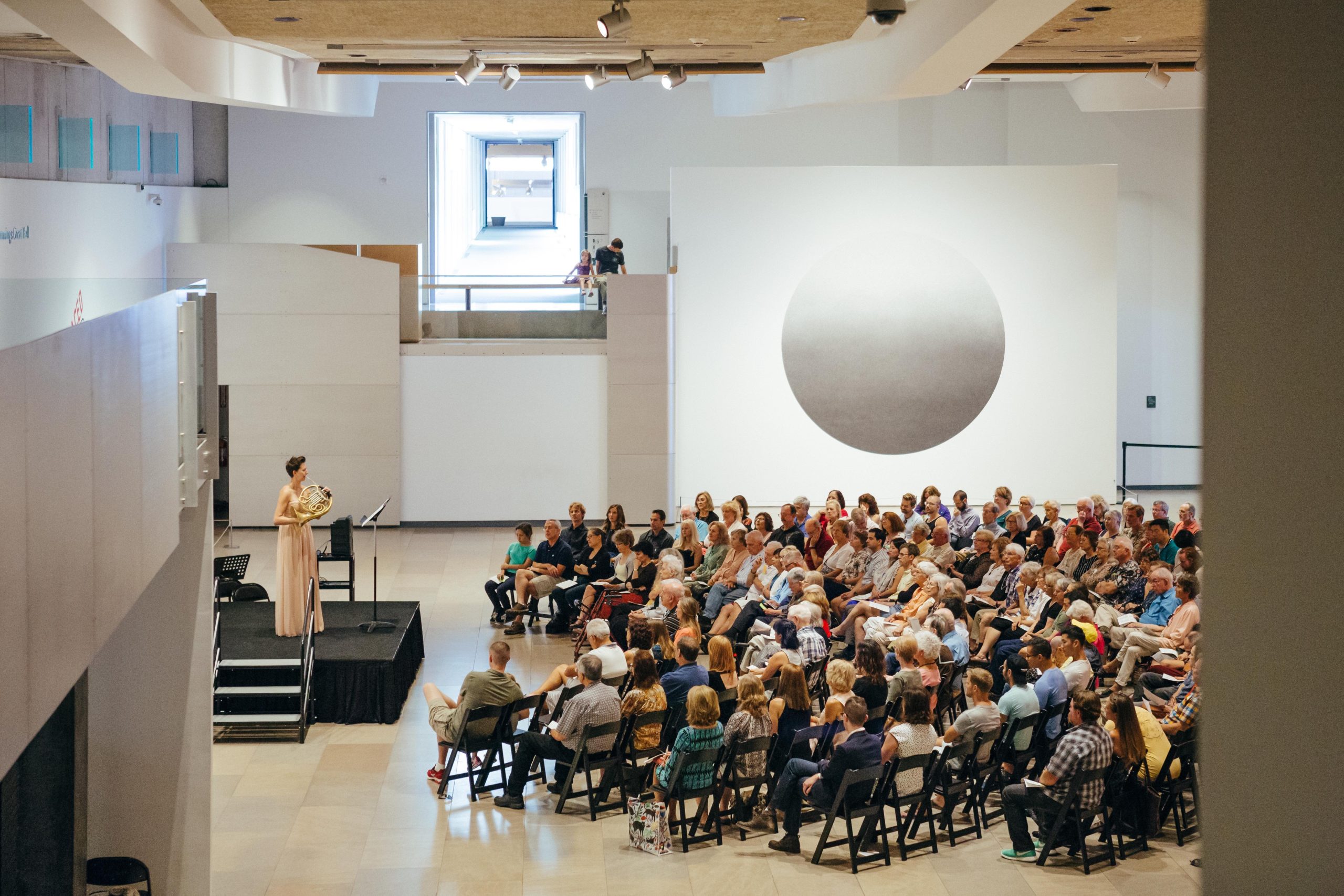 Solo horn performance with a large audience at an art museum