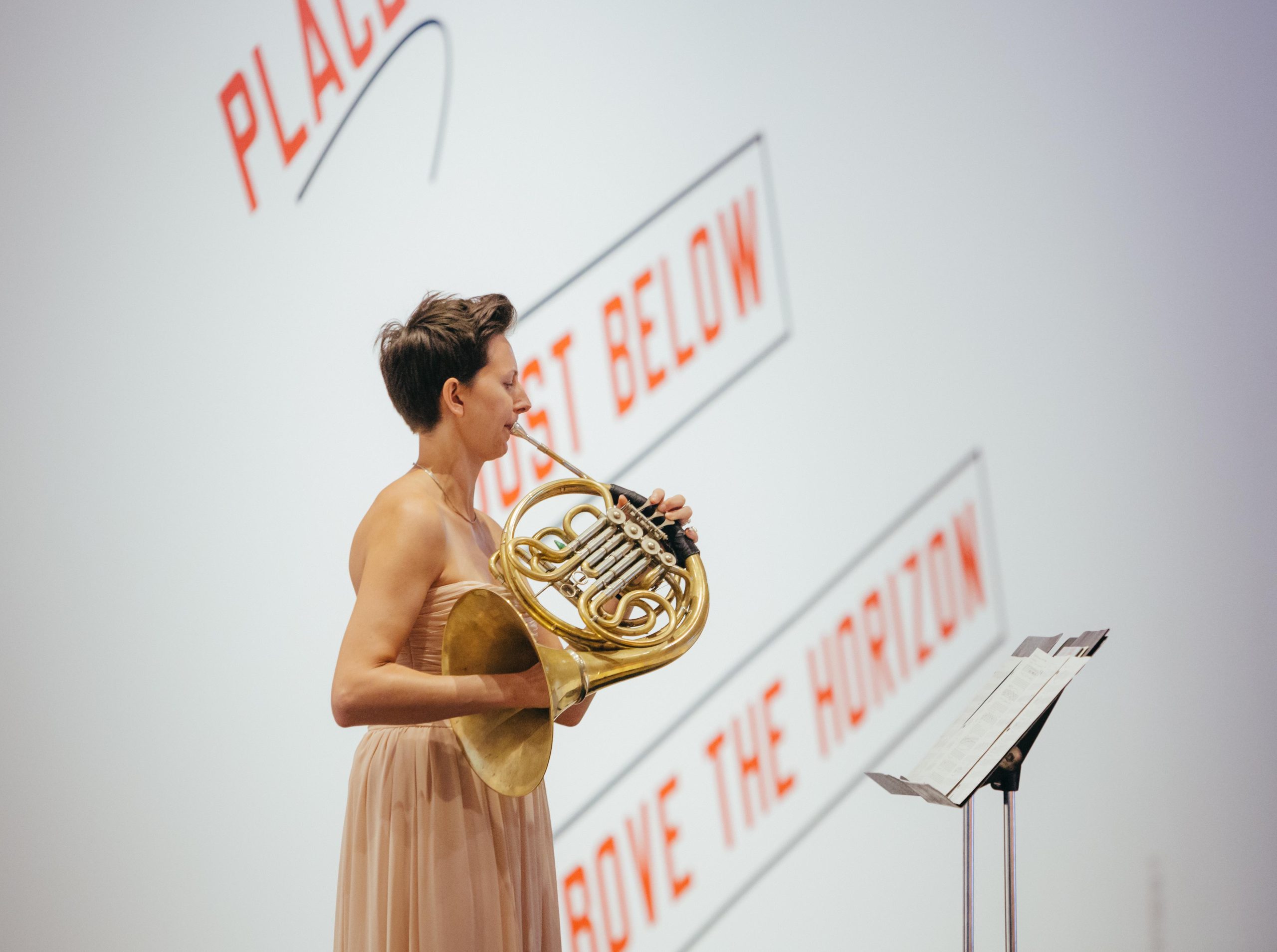 Woman plays French horn in front of modern art